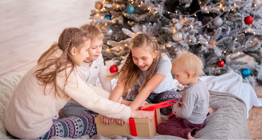 Siblings opening a gift next to a Christmas tree.
